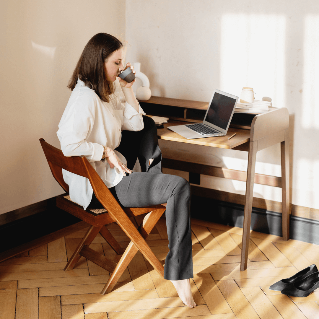 Woman sitting at desk drinking a hot beverage and looking at computer